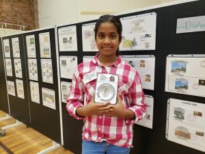 a little girl standing in a room: Youngest TNC member, Sahitya at TALPEX 2019 holding 5 oz. 50th Anniversary Moon Landing silver coin released by US mint in 2019